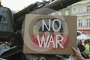 Woman holding poster with words No War near broken military tank on street, closeup
