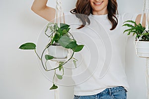 Woman holding pots with plans by a macrame pot-holders over white wall