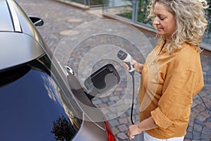 Woman holding power supply cable at electric vehicle charging station, closeup