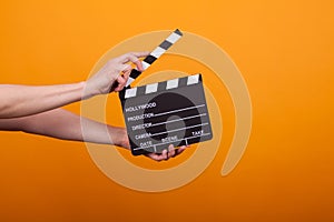 Woman holding professional film slate, movie clapper board in studio over yellow background