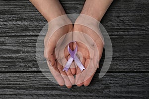 Woman holding purple awareness ribbon on black wooden background