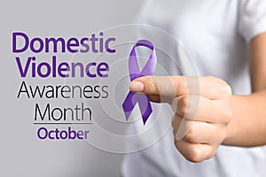 Woman holding purple ribbon on background, closeup. Symbol of Domestic Violence Awareness