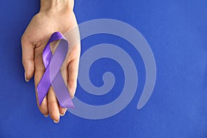 Woman holding purple ribbon on color background. Pancreatic cancer awareness concept