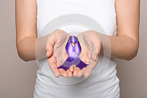 Woman holding purple ribbon on grey background. Domestic violence awareness