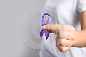Woman holding purple ribbon on grey background. Domestic violence awareness