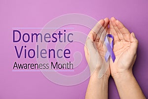 Woman holding purple ribbon on lilac background. Symbol of Domestic Violence Awareness