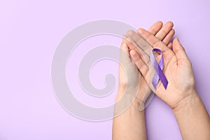 Woman holding purple ribbon on lilac background, top view. Domestic violence awareness