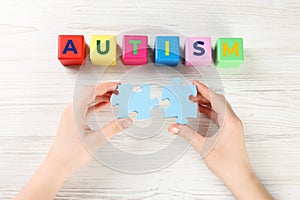 Woman holding puzzle pieces near cubes with word Autism at white wooden table, top view
