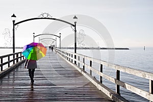 Woman holding a rainbow colored umbrella walking on a rainy day.