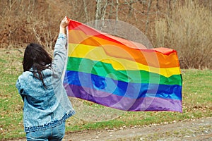 Woman holding the rainbow flag on the nature. Happiness, freedom and love concept for same sex couples