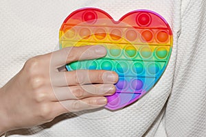 Woman holding rainbow heart in her hand close up. LGBT or GLBT concept. Pop Fidget Sensory Toy for Autism Special Needs