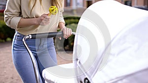 Woman holding rattle toy front of newborn in stroller, babyhood interaction