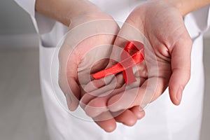 Woman holding red awareness ribbon indoors, closeup. World AIDS disease day