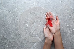 Woman holding red awareness ribbon at light grey marble table, top view with space for text. World AIDS disease day