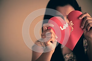 Woman holding red broken heart with love text.