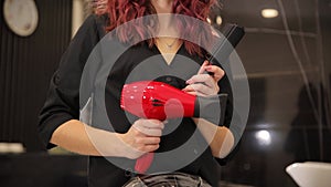 A woman is holding a red hair dryer and a curling iron