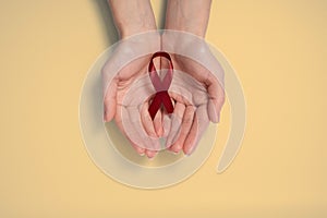 Woman holding red ribbon as symbol of World Cancer Day, on yellou background, cancer awareness sign.