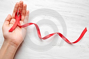 Woman holding red ribbon on white wooden background. AIDS concept