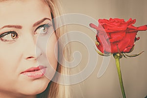 Woman holding red rose near face looking melancholic