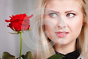 Woman holding red rose near face looking melancholic
