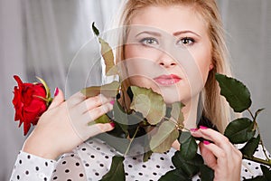 Woman holding red rose near face looking melancholic