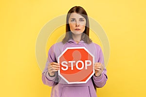 Woman holding red stop sign, looking at camera strict expression, prohibition.