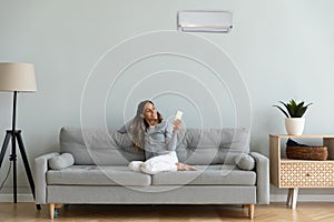 Woman holding remote control manages degrees enjoy air-conditioned flat