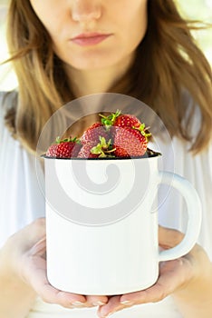 woman holding ripe strawberries in an enamel mug