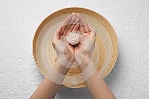 Woman holding rose flower above bowl with water on white towel, top view