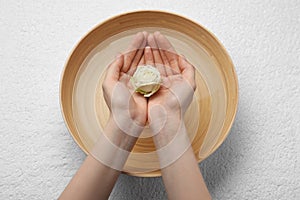 Woman holding rose flower above bowl with water on white towel, top view