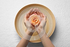 Woman holding rose flower above bowl with water on white towel, top view