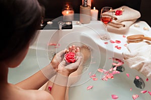 Woman holding rose flower while taking bath, closeup. Romantic atmosphere