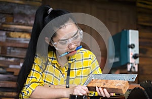 Woman holding ruler and pencil while making marks on the wood the table in the workshop