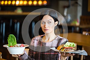 Woman holding a salad and a burger.Woman choosing between healthy and unhealthy eating