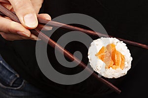 Woman holding a salmon maki sushi piece with chopsticks