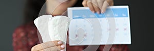 Woman holding sanitary pads and calendar with red numbers closeup