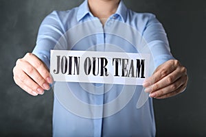 Woman holding sheet of paper with words JOIN OUR TEAM on grey background. Career concept