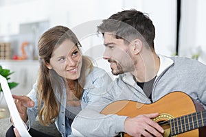 woman holding sheetmusic for man playing guitar