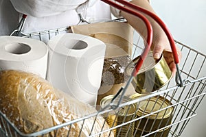 Woman holding shopping basket with products and toilet paper rolls. Panic caused by virus