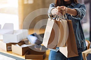 A woman holding and showing shopping bags with tablet pc and postal parcel box on the table for online shopping