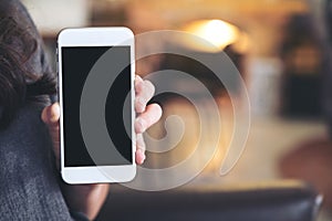 A woman holding and showing white mobile phone with blank black screen in cafe