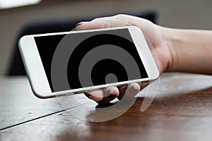 A woman holding and showing white mobile phone with blank black screen for watching on wooden table