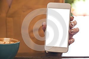 A woman holding and showing white mobile phone with blank desktop screen with coffee cup on wooden table