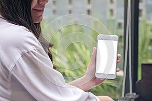 A woman holding and showing white mobile phone with blank screen in cafe