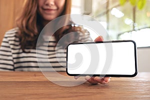 A woman holding and showing white mobile phone with blank screen horizontally on wooden table