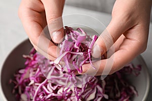 Woman holding shredded fresh red cabbage at grey table, closeup