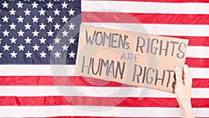 Woman is holding a sign Womens Rights Are Human Rights US flag on background