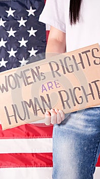 Woman is holding a sign Womens Rights Are Human Rights US flag on background