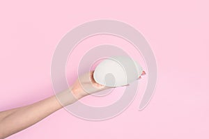 Woman holding silicone implant for breast augmentation on color background, space for text