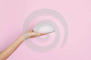 Woman holding silicone implant for breast augmentation on color background, space for text.